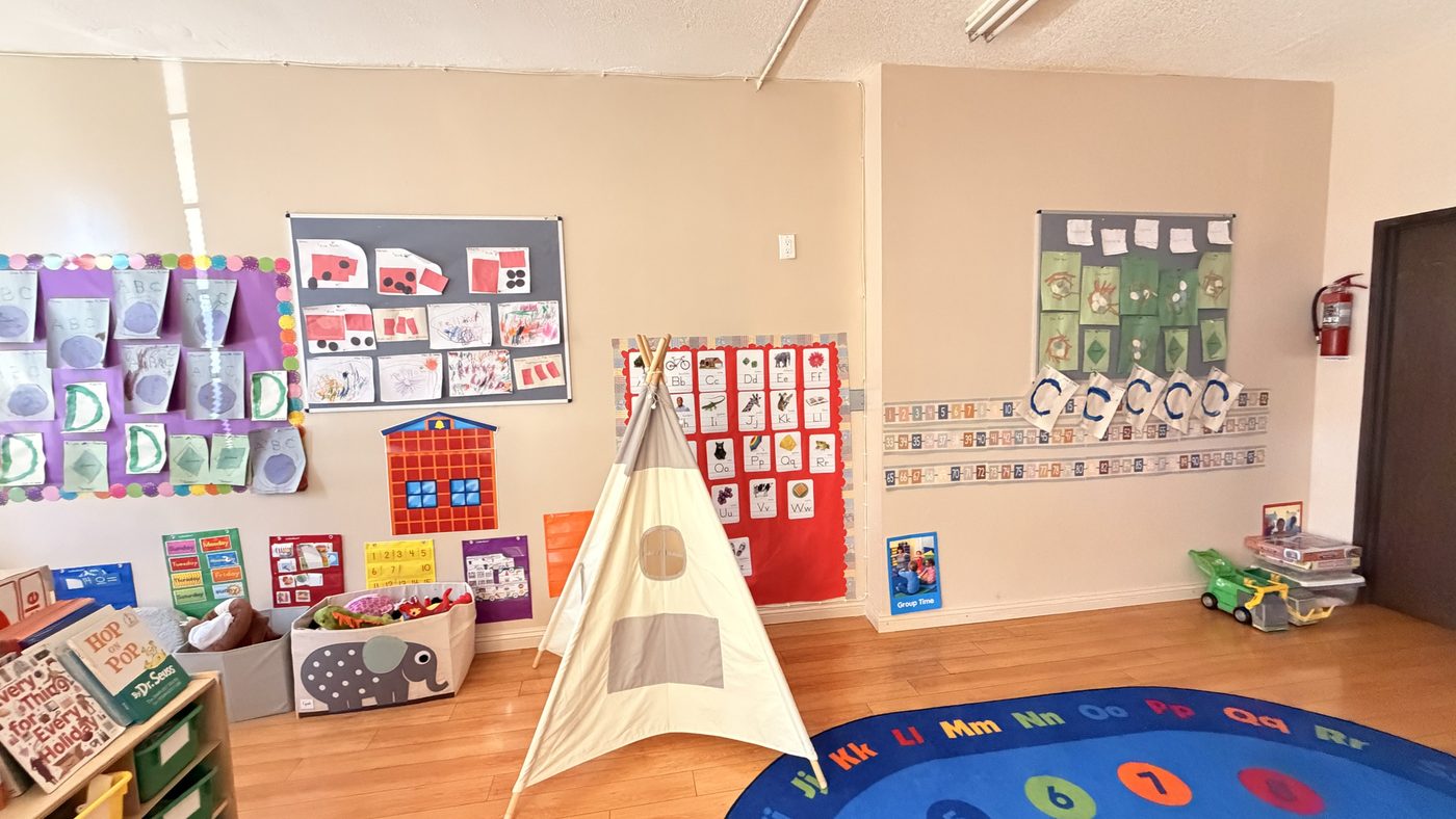A Sunshine Child Care Center classroom, with children's artwork on the walls, a reading teepee and an alphabet rug.